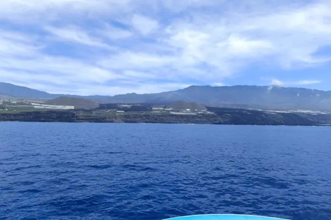 Blue ocean with distant mountainous shoreline under a partly cloudy sky.